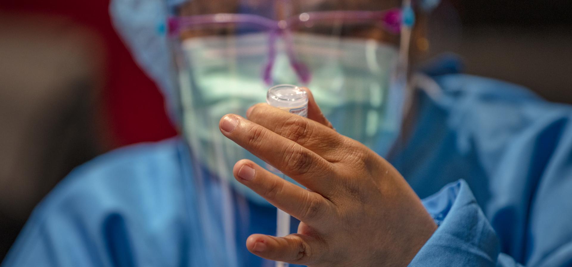 Person in blue medical scubs draws a vaccine from a vile into a syringe