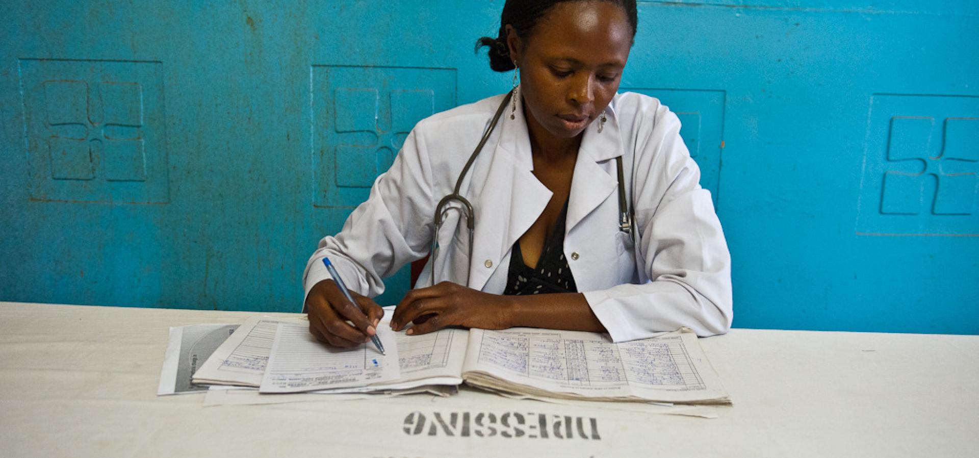 African woman wearing a white lab coat looks down at paperwork