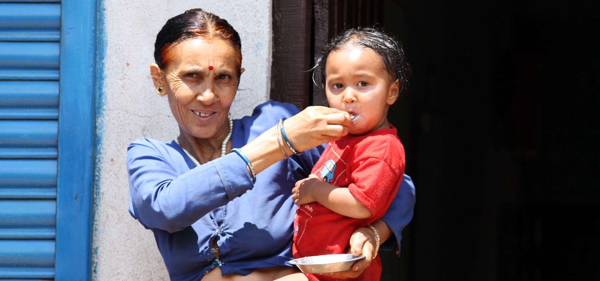 Grandmother holds child and spoon feeds her