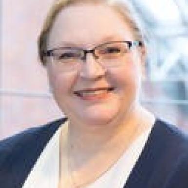 Woman wearing a white shirt, blue blazer, and glasses looks into the camera