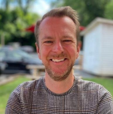 Man smiles into the camera, standing outside