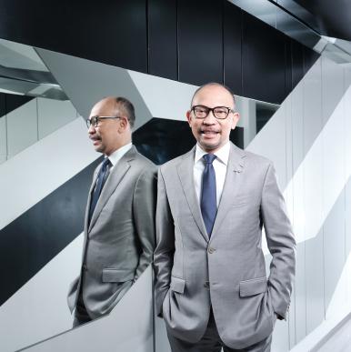 Man wearing glasses and a gray suit, stands in front of a modern mirror