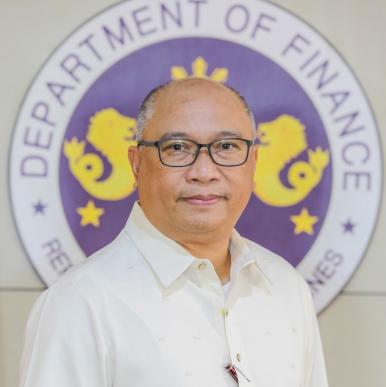 Man wearing a white shirt and glasses stands in front of a Department of Finance sigil