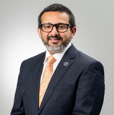 Man wearing a dark blue suit, wearing glasses, looks into the camera