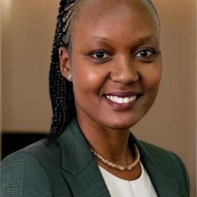 Woman with braided hair pulled back, wearing a gray blazer, smiles into the camera