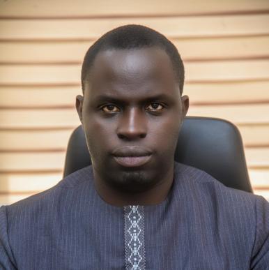 African man wearing a dark blue shirt, looks into the camera