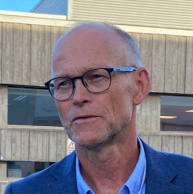 Norwegian man with glasses, wearing a blue suit jacket, looks to the left of the camera