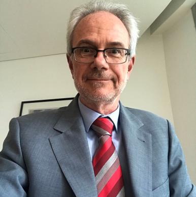 Man with grey hair wearing a grey suit with a red and grey striped tie