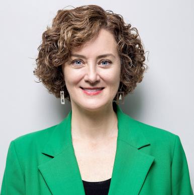 Woman with short red hair smiles into the camera, wearing a bright green blazer