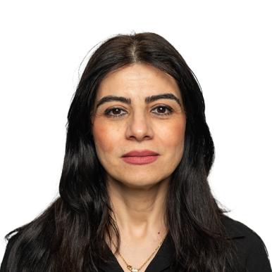 Woman with dark brown hair, standing in front of a white background, looks into the camera