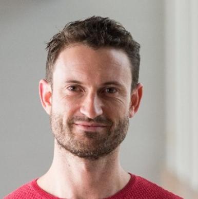 Man with a short beard, wearing a red t-shirt, smiles into the camera