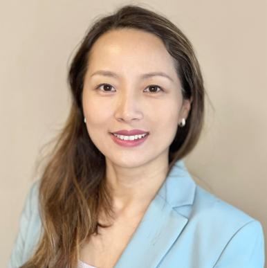 Asian woman with light brown hair, wearing a light blue blazer, smiles into the camera