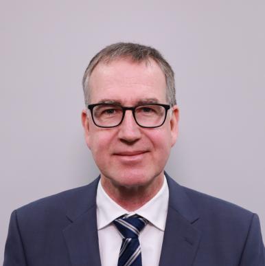 Man wearing a blue suit and black glasses looks into the camera