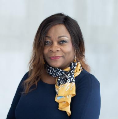 Woman wearing a blue shirt and yellow neck scarf smiles into the camera