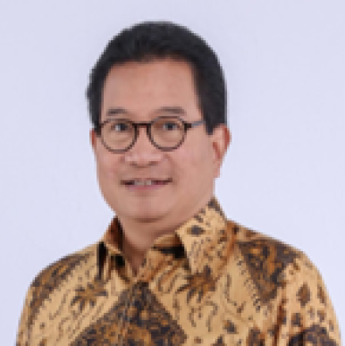 Man wearing a shirt with a traditional pattern on it, and glasses, smiles into the camera