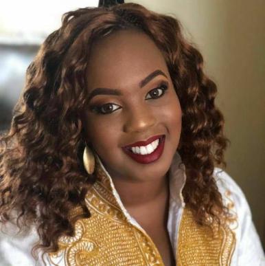 Angela Gichaga headshot Woman with dark curls smiles into the camera