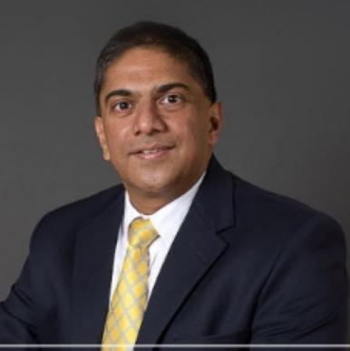 Neren Rau headshot Man wearing a black suit with a yellow tie looks into the camera