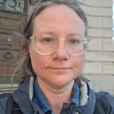 Olya Golichenko headshop White woman wearing clear glasses and a blue winter jacket looks into the camera