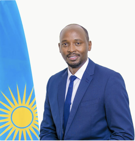 African man wearing a blue blazer looks into camera, with the flag of Rwanda off his right shoulder