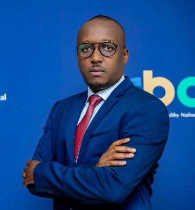 Rwandan man wearing glasses, stands in a bright blue suite with a red tie, against a backdrop that says RBC