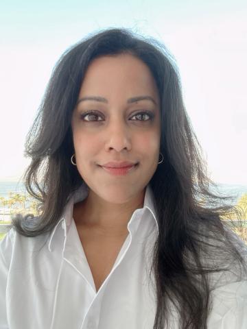 Headshot of a woman with long brown hair, looking directly into the camera, wearing a white collared shirt