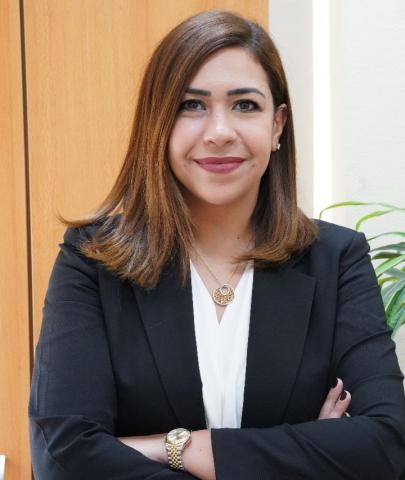 Woman with light brown hair, in a black blazer, crosses her arms and smiles into the camera 