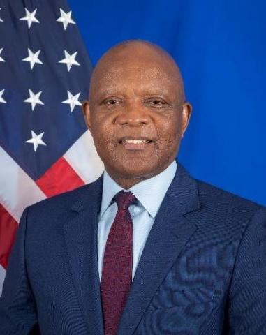 Man in a blue suit stands in front of an American flag