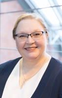 Woman wearing a white shirt, blue blazer, and glasses looks into the camera