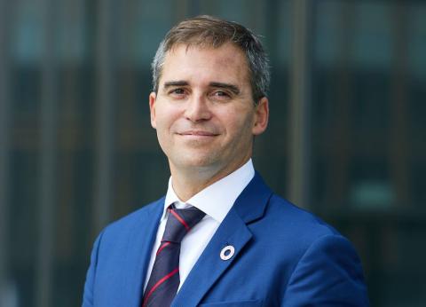 Man in a blue suit, with an SDG pin, stands and looks into camera