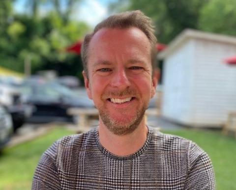 Man smiles into the camera, standing outside