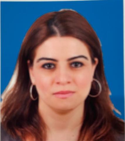 Woman with red/brown hair wearing hoop earrings, looks into the camera in front of a blue backgrop