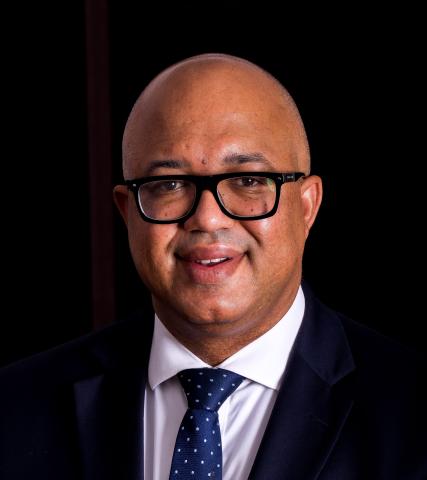 Man wearing glasses, wearing a black suit and blue tie, stand in front of a black background