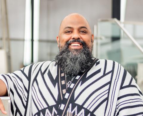 Man with beard, wearing a long shirt with a traditional African design, smiles into the camera