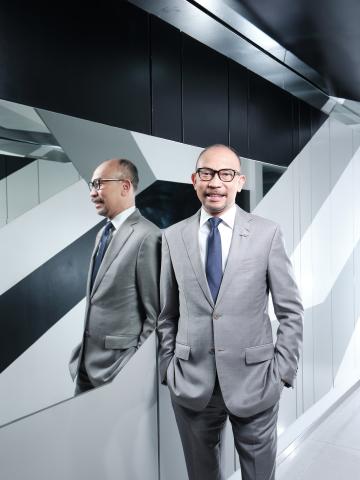 Man wearing glasses and a gray suit, stands in front of a modern mirror