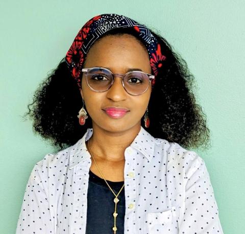 Woman with dark curly hair looks into the camera, wearing glasses, a colorful headband, and dotted shirt