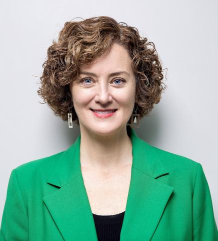 Woman with short red hair smiles into the camera, wearing a bright green blazer