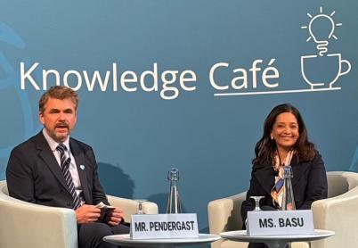 Priya Basu and Scott Pendergast sit in front of a backdrop which reads Knowledge Café, with a lightbulb over a mug