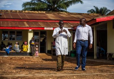 Two men walk and talk in front of a house