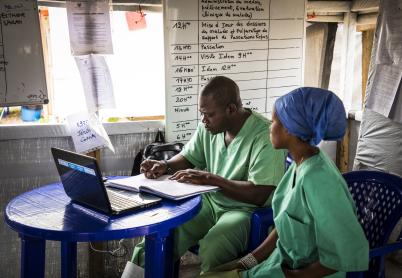 Two heath workers wearing scrubs research on a laptop