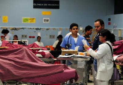 Health workers look over paperwork while patients lie in hospital beds. The words Clinica de medicina are written on the wall behind them