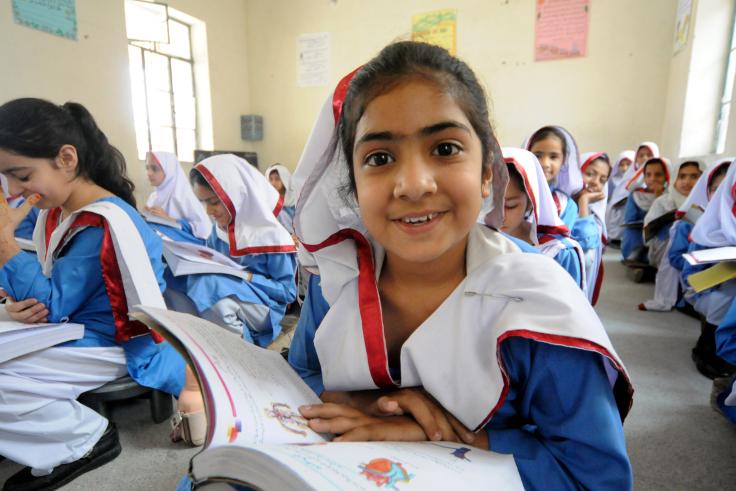 Young girl looks up from a book and smiles into the camera, wearing a white and blue uniform