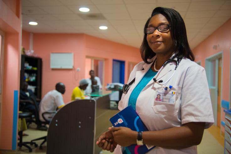 African woman in white shirt, wears glasses and a stethoscope around her neck