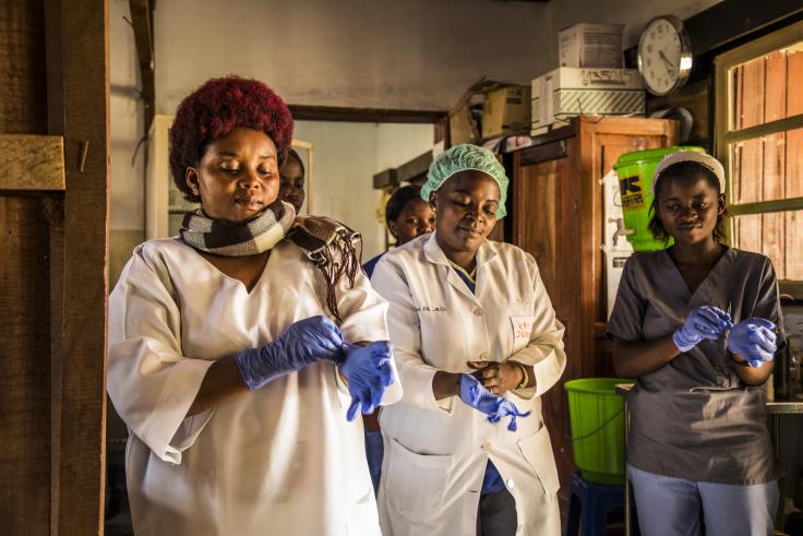 Three women in white lab coats put on blue gloves