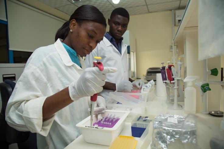 Woman in white lab coat conducting experiment with dropper into container