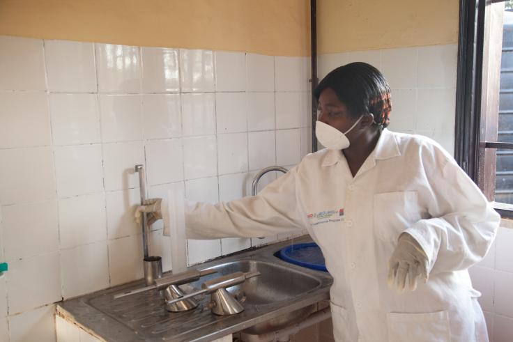 Woman in a white lab coat and N95 mask turns on water