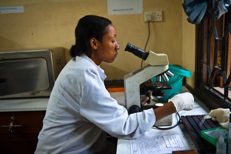 Woman in a white lab coat looks into a microscope