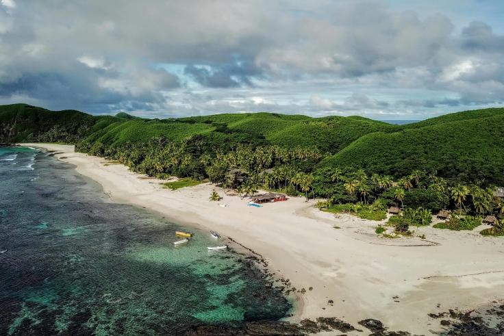 Blue water, sandy beach, green rolling hills in Fiji