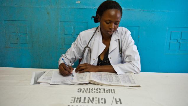 African woman wearing a white lab coat looks down at paperwork