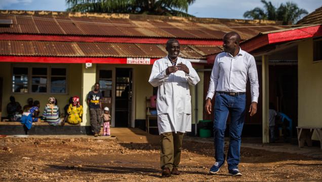 Two men walk and talk in front of a house